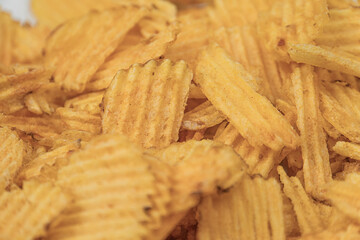 Close-up view of a pile of crispy yellow potato chips with ridges, under bright indoor lighting...