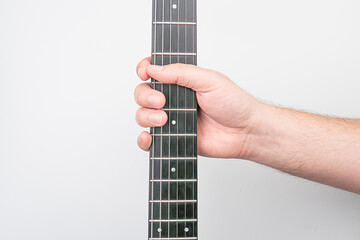 Close-up view of a hand on a silver guitar neck with tuning pegs and frets, against a plain...