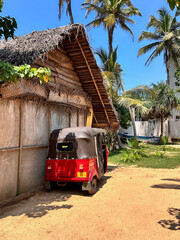  small three-wheeled tented vehicle stands by a wooden shed on a tropical island on a sunny day.