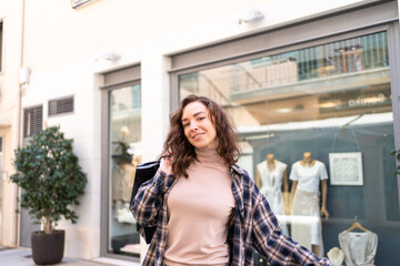 Fototapeta premium Stylish woman with shopping bags walking outside a fashion boutique, enjoying a shopping day in the city.