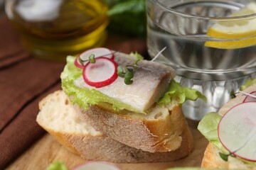 Tasty sandwiches with herring, radish and lettuce on table, closeup
