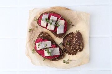 Tasty sandwiches with herring and horseradish sauce on white tiled table, top view
