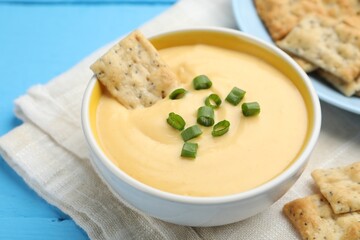 Tasty cheese dipping sauce in bowl and crackers on light blue wooden table, closeup
