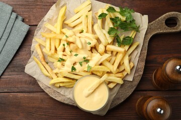 Delicious cheese sauce in bowl, French fries and parsley on wooden table, flat lay