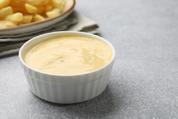 Tasty cheese sauce in bowl and French fries on grey table, closeup. Space for text