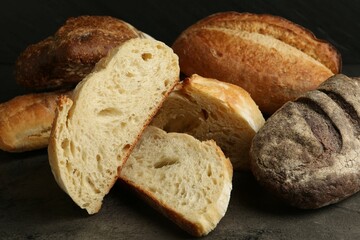 Different types of fresh bread on dark textured table against black background, closeup