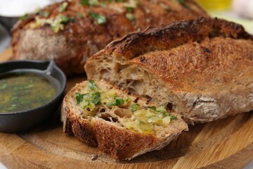 Tasty bread with garlic, herbs and oil on table, closeup