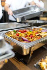 Caterers preparing a buffet with grilled vegetables and meats in a modern dining setting