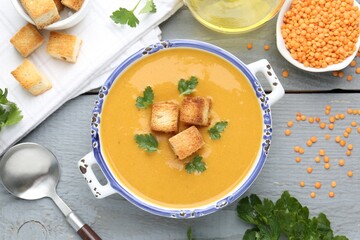 Delicious lentil cream soup served with croutons on grey wooden table, flat lay