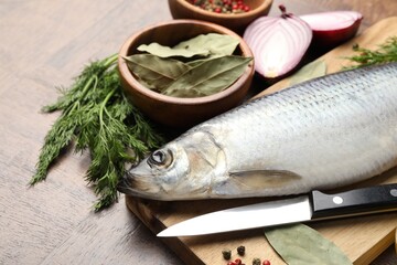 Salted herring, spices and knife on wooden table, closeup