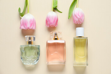 Bottles of perfume and beautiful flowers on beige background, flat lay