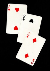 A hand of three playing cards of the same value isolated on a black background.