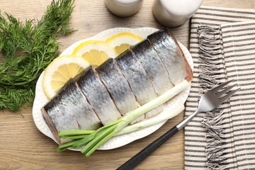 Pieces of delicious herring with lemon slices, green onions and dill on wooden table, flat lay