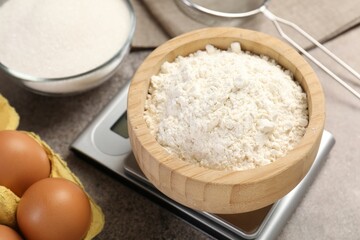 Digital kitchen scale with bowl of flour and other products on grey textured table, closeup
