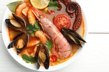 Delicious seafood soup in bowl on white wooden table, top view