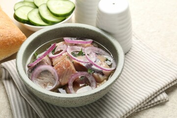 Pieces of delicious herring with onions, cucumber slices and bread on light table, closeup
