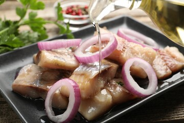 Pouring oil onto pieces of herring with onions at wooden table, closeup