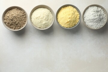 Different types of flour in bowls on light grey table, flat lay. Space for text