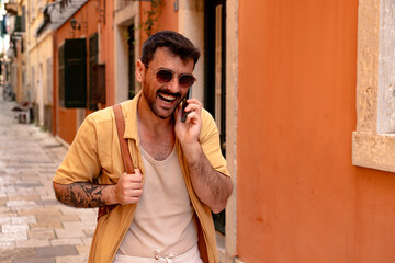 Happy tourist walking and chatting on the phone while enjoying a picturesque street filled with...