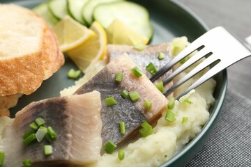 Pieces of delicious herring, mashed potato, cucumber slices and bread served on black table, closeup