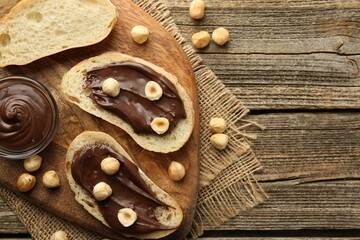 Slices of bread with chocolate spread and hazelnuts on wooden table, flat lay. Space for text