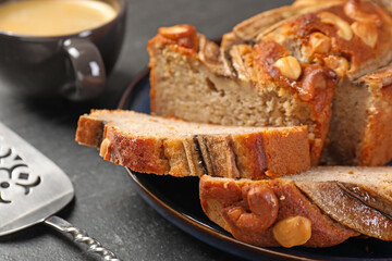 Cut banana bread with nuts, server and coffee on black table, closeup