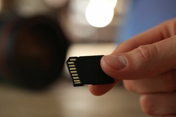 Man with SD memory card on blurred background, closeup. Space for text