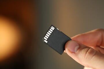 Man with SD memory card on blurred background, closeup. Space for text
