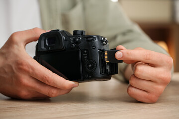 Man inserting SD memory card into photo camera at wooden table indoors, closeup