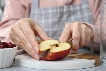 Woman cutting apples at light grey table, closeup