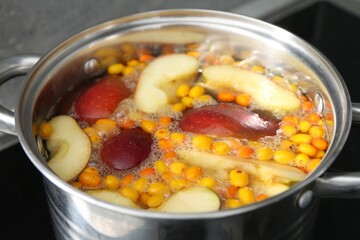 Making compot of apples and sea buckthorn berries. Simmering fruits in pot on stove, closeup