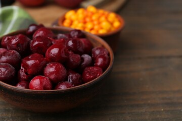 Tasty cherries and sea buckthorn berries on wooden table, closeup. Space for text