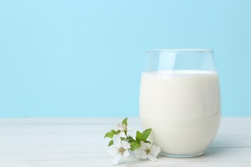Glass of fresh milk and blossoms on white wooden table against light blue background. Space for text