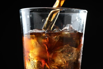 Pouring refreshing cola into glass on black background, closeup