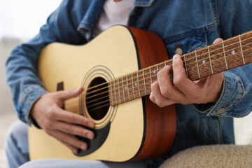 Fototapeta premium Man playing guitar on armchair indoors, closeup