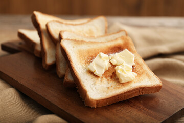 Crispy toasts with butter on wooden board, closeup