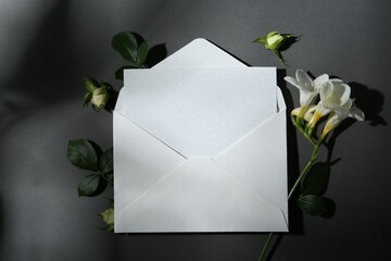 Blank greeting card in envelope and freesia flowers on dark grey background, flat lay