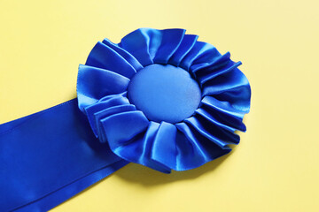 Blue award ribbon on yellow background, closeup