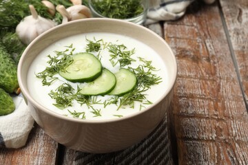 Tasty cucumber soup in bowl and ingredients on wooden table, closeup