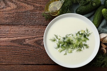 Tasty cucumber soup in bowl and ingredients on wooden table, flat lay. Space for text