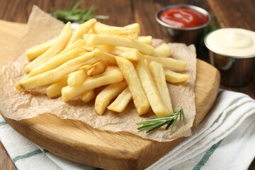 Tasty french fries served with sauces and rosemary on wooden table, closeup
