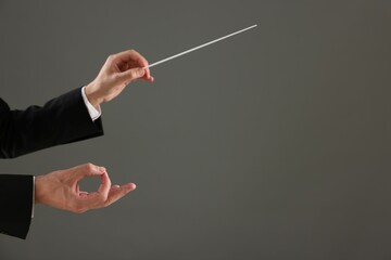 Professional conductor with baton on grey background, closeup. Space for text