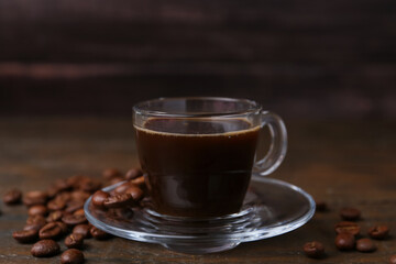Aromatic coffee in glass cup and beans on wooden table, closeup