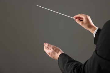 Professional conductor with baton on grey background, closeup. Space for text
