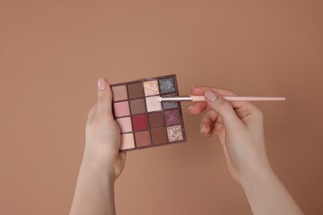 Woman with eyeshadow palette and brush on beige background, closeup