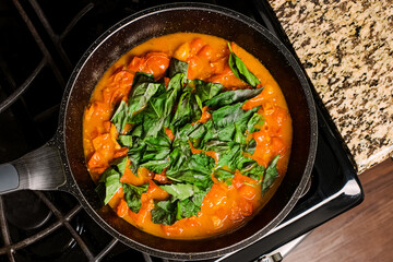 Cooking fresh tomato basil sauce in a skillet on a modern kitchen stove,