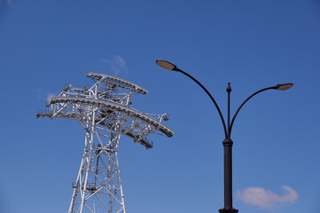 Cableway support tower against blue sky. Construction of cross-border cableway between Russia and China. Support made of white pipes in Blagoveshchensk. Street lamp in the foreground in blur.