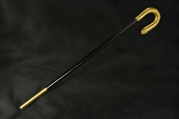 Elegant gold and black walking stick on dark fabric background; perfect for elderly care, fashion, or historical themed projects