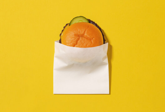 Blank white paper burger wrap packaging mockup for  fast food restaurant branding or logo presentation isolated on a vibrant yellow studio background