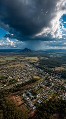 Obraz premium Aerial view of a town nestled below a dramatic storm cloud. A mountain peak is visible in the distance